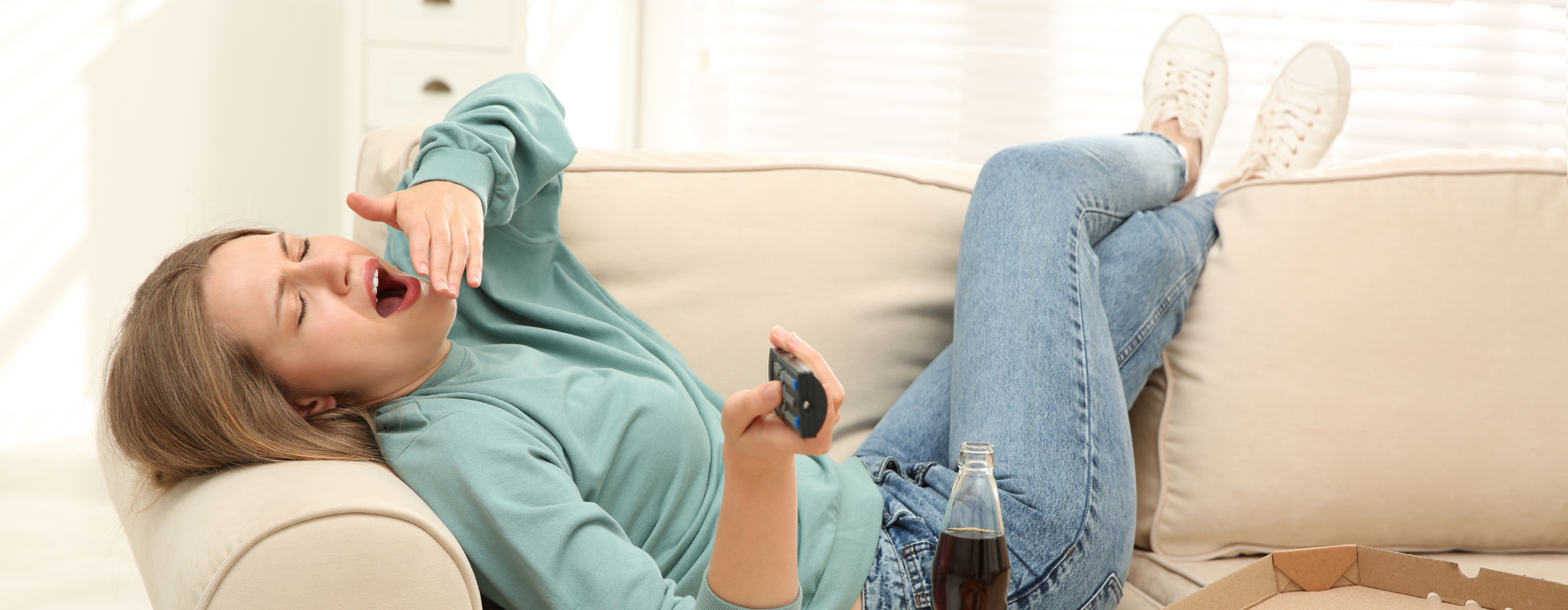 Mulher deitada no sofá com diversos alimentos na mesinha, simbolizando o sedentarismo e seus impactos no estilo de vida.