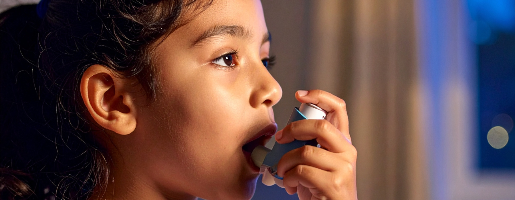 Menina com asma infantil usando a bombinha para melhorar a respiração durante uma crise.