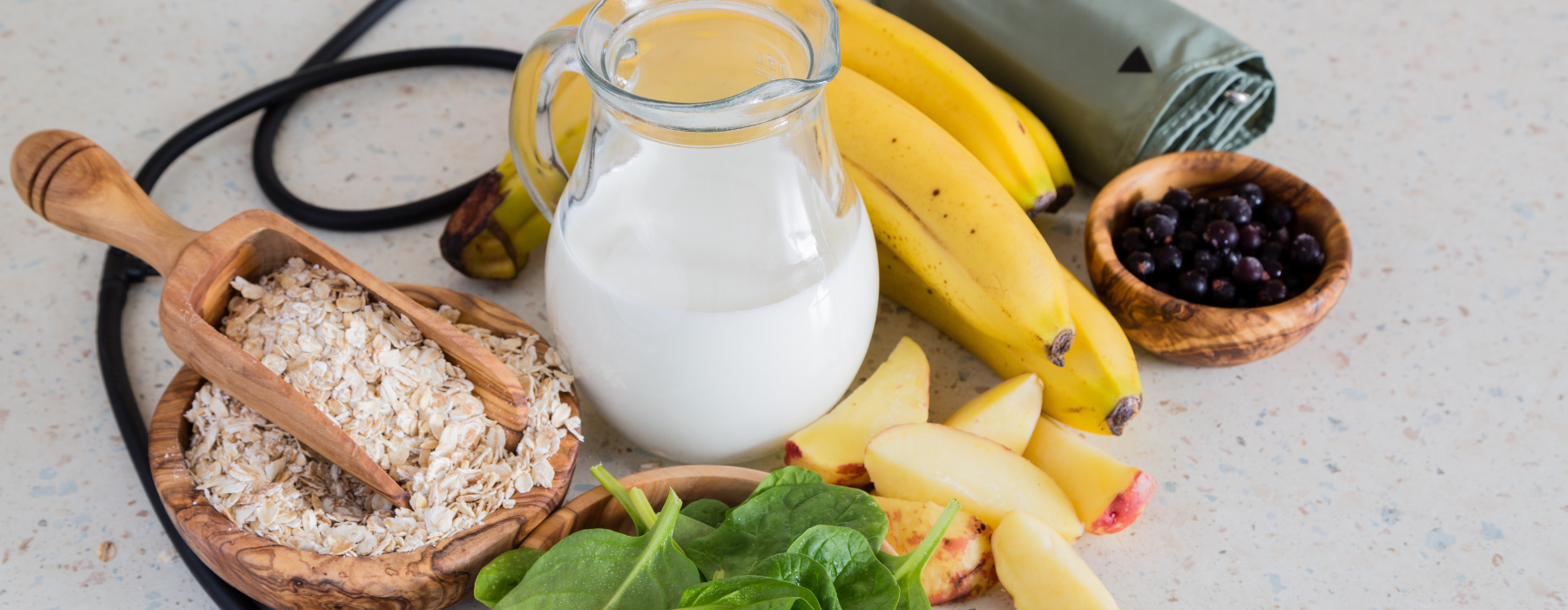 Alimentos saudáveis como banana, leite, aveia, espinafre e frutas sobre a mesa