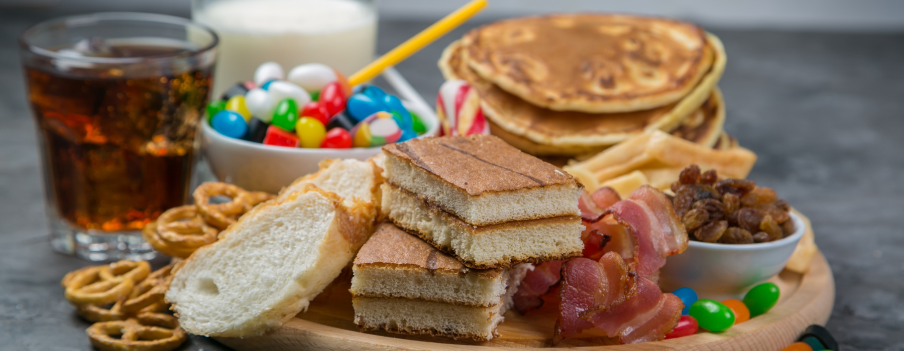 Prato com pães, doces, refrigerante, balas, panquecas e bacon sobre uma mesa.