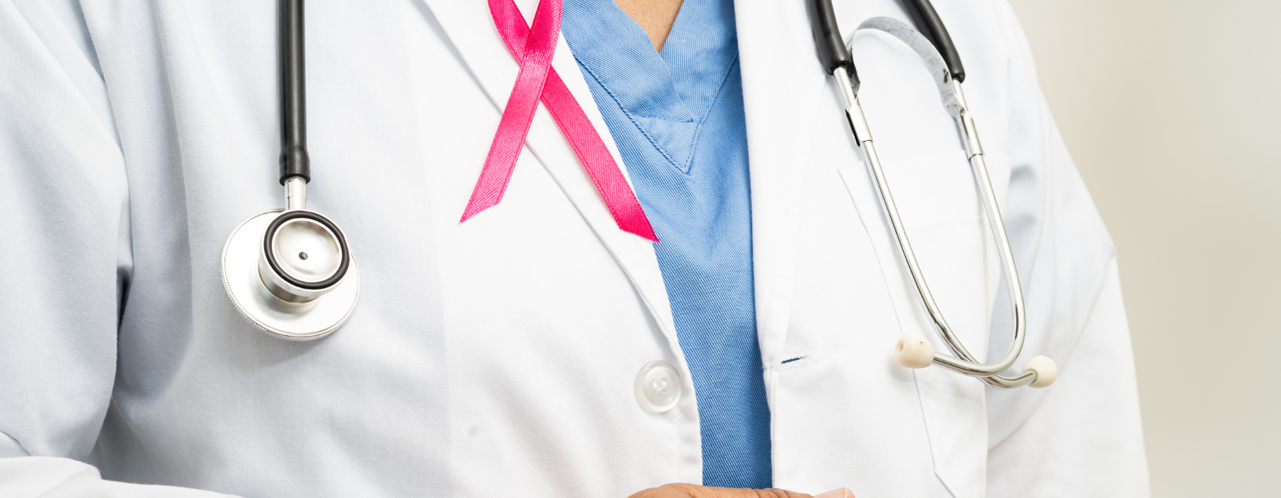 Médico com jaleco branco e estetoscópio usa laço rosa para apoiar a conscientização sobre o câncer de mama masculino.