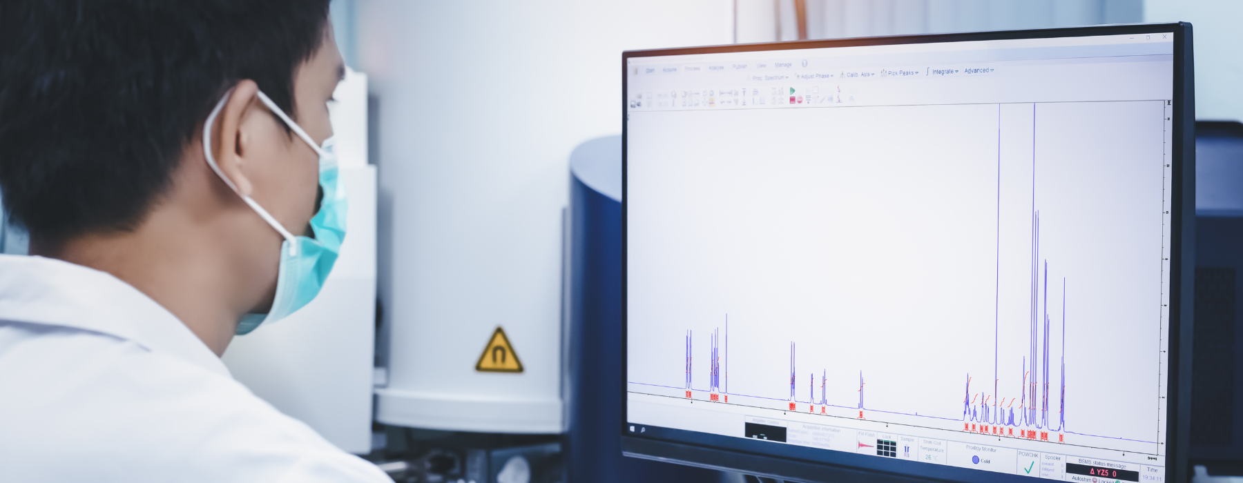 Profissional de saúde usando máscara analisa imagens médicas em monitor durante exame de Ressonância Multiparamétrica.