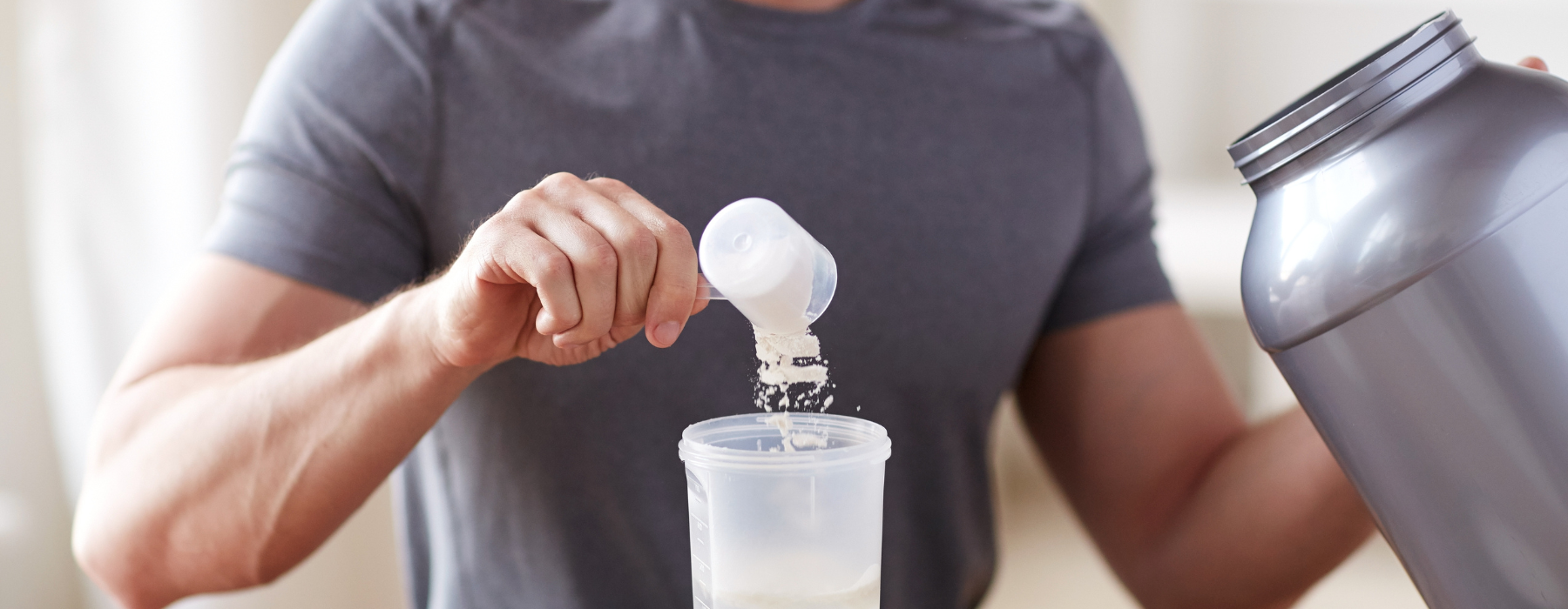 Pessoa adicionando creatina em pó em um shaker enquanto segura um pote grande de suplemento.