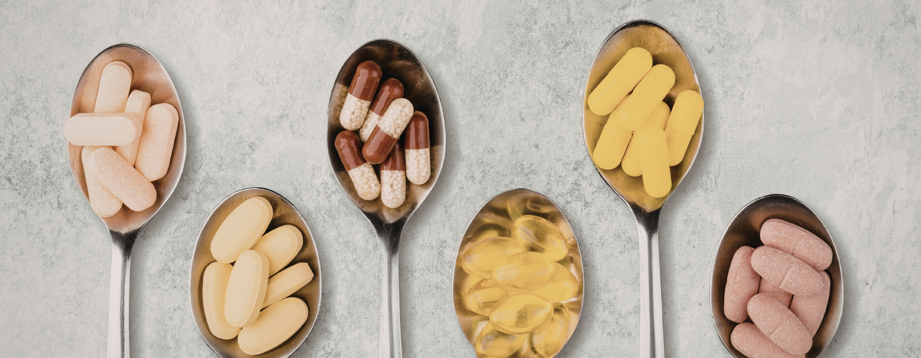 Colheres com cápsulas e comprimidos de suplementos, representando opções de vitamina B12.