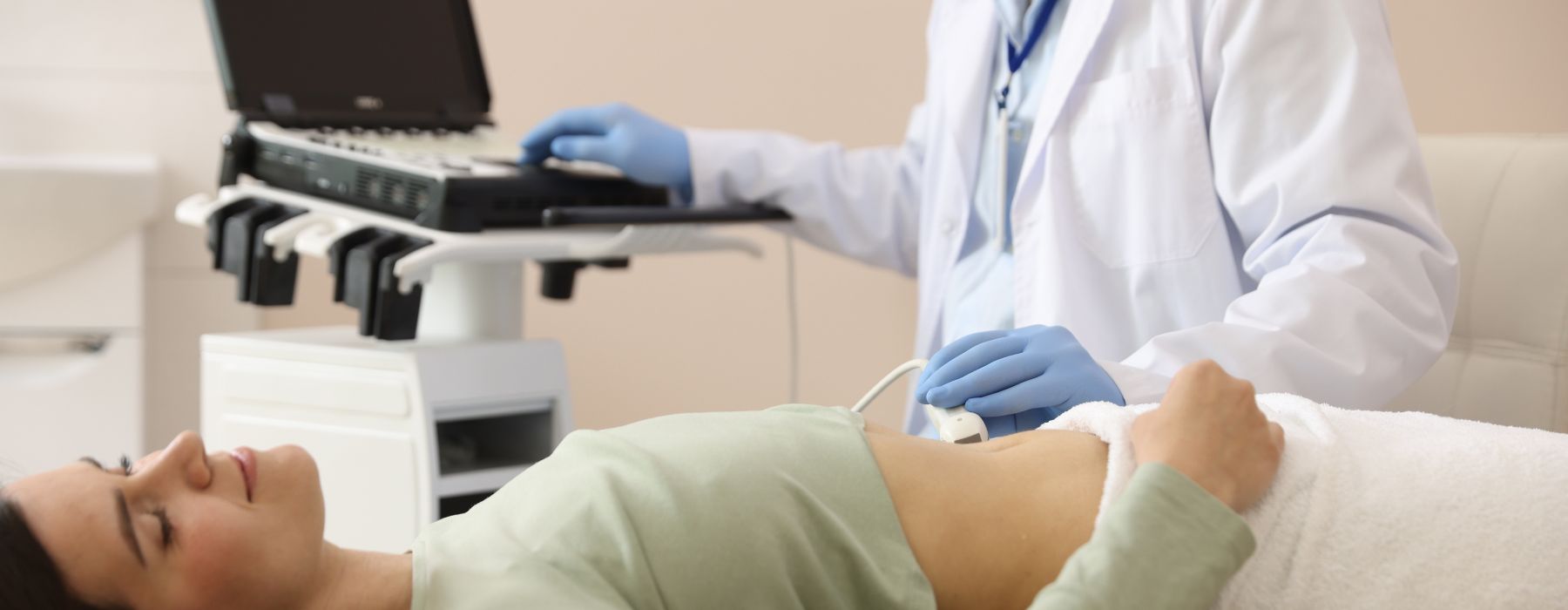 Médico realizando um exame de ultrassom abdominal em paciente feminina, deitada na maca. Médio de jaleco e paciente de blusa verde e calça branca. 