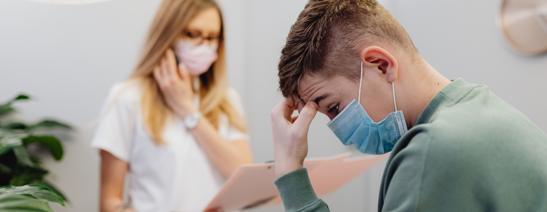 Homem usando máscara durante consulta médica, demonstrando mal-estar enquanto uma profissional de saúde realiza o atendimento.