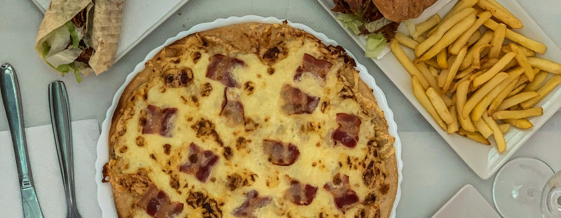 Pizza, batatas fritas, hambúrguer e wrap sobre uma mesa, representando alimentos associados ao aumento do risco de obesidade infantil.